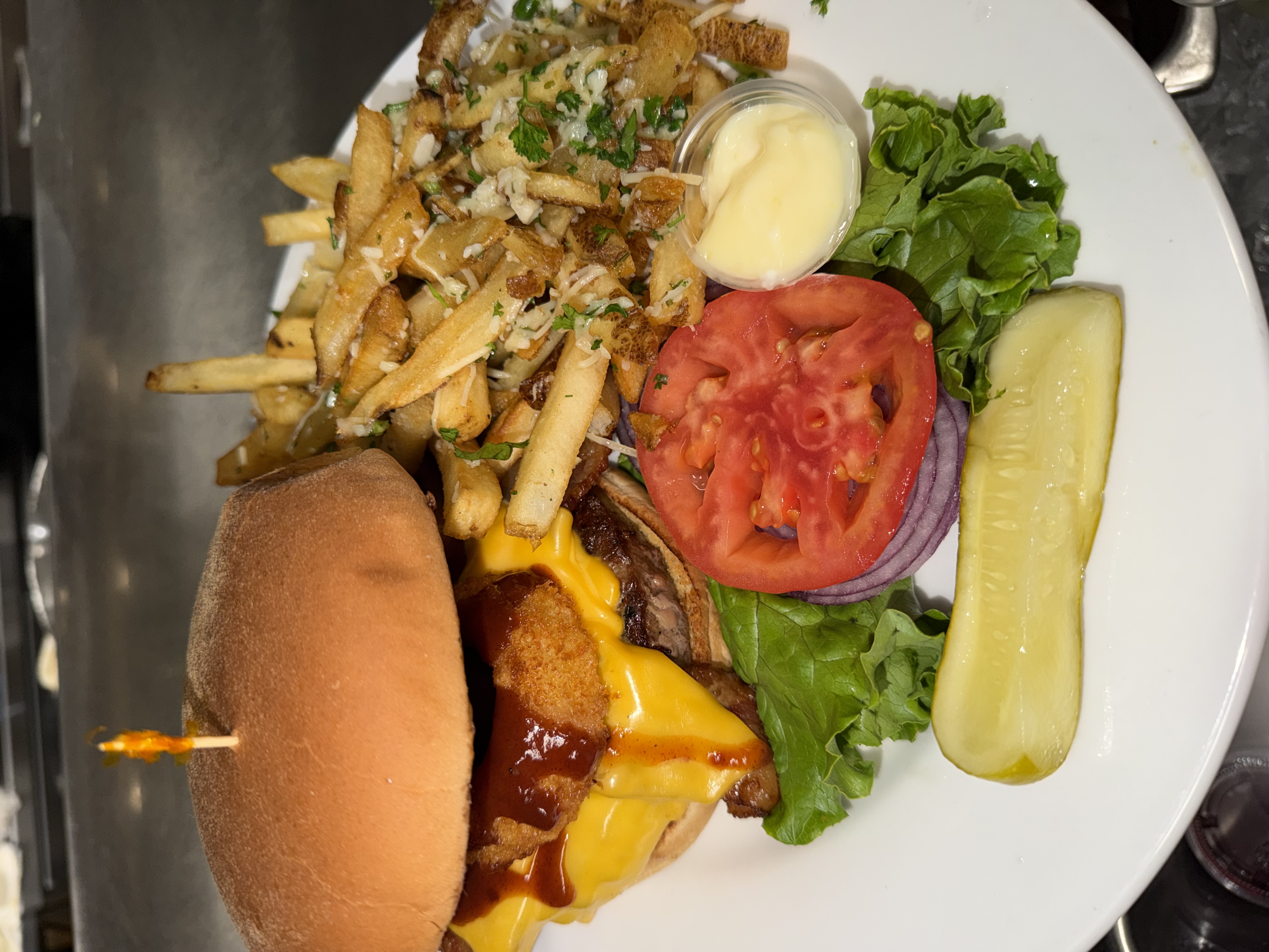Sierra Grill Smokehouse signature burger with melted cheese, onion rings, BBQ sauce, seasoned fries, and fresh garnish