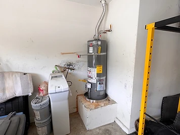 Newly installed gas water heater on a raised garage pedestal with copper piping and a water softener beside it.