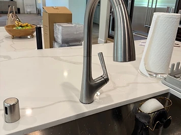Brushed-nickel, single-handle kitchen faucet newly installed on a white quartz countertop above a stainless sink.