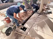 Two plumbing technicians excavating a trench in a residential driveway