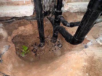 Black drain pipes and copper supply lines exposed in an opened concrete slab during a drain-line repair.