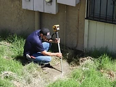 Second Opinion Plumbing technician kneeling beside a building, removing standing water during a leak repair.