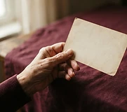 An elderly hand holding a postcard
