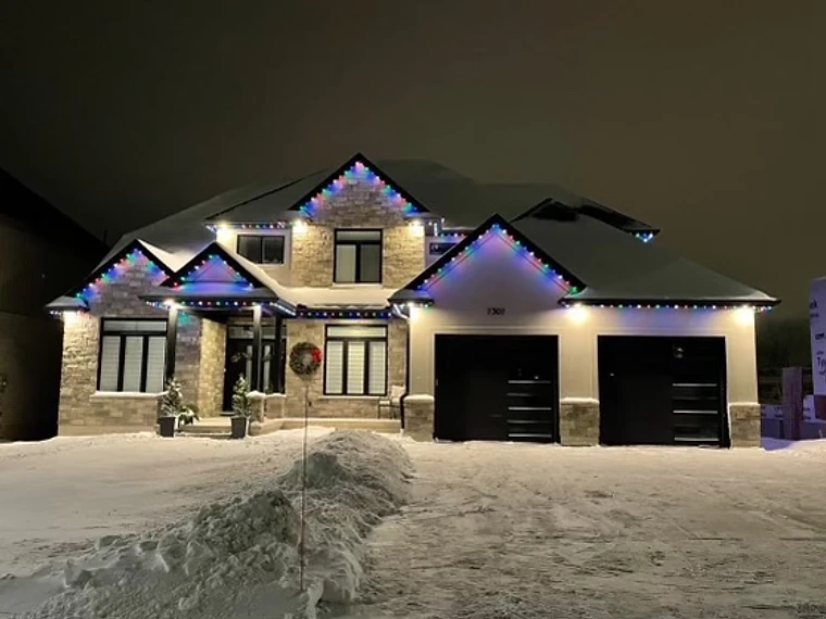 Color-changing permanent LED roofline lighting on a stone home at night