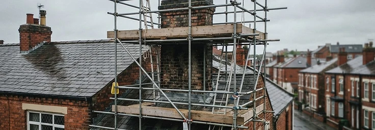 Scaffolding erected around a chimney stack on a slate roof of an older brick house
