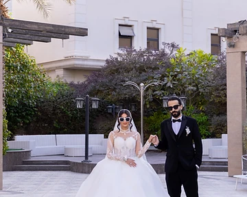 Bride and groom holding hands in a sunlit courtyard with palm trees
