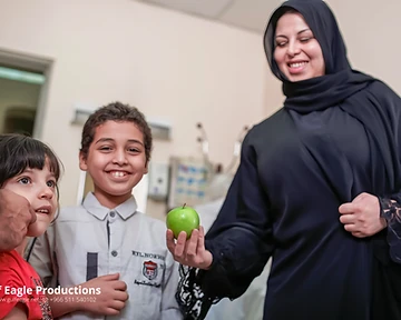 Nutritionist offering fruit to children during a health awareness campaign shoot in Riyadh