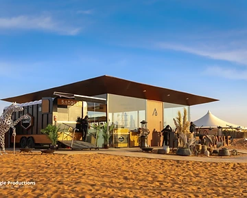 Modern modular desert venue building with glass walls and camel sculpture in a sand dune landscape
