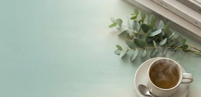 Calming wellness scene with stacked books, eucalyptus, and herbal tea