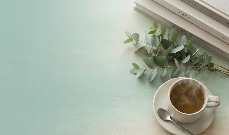 Calming wellness scene with stacked books, eucalyptus, and herbal tea