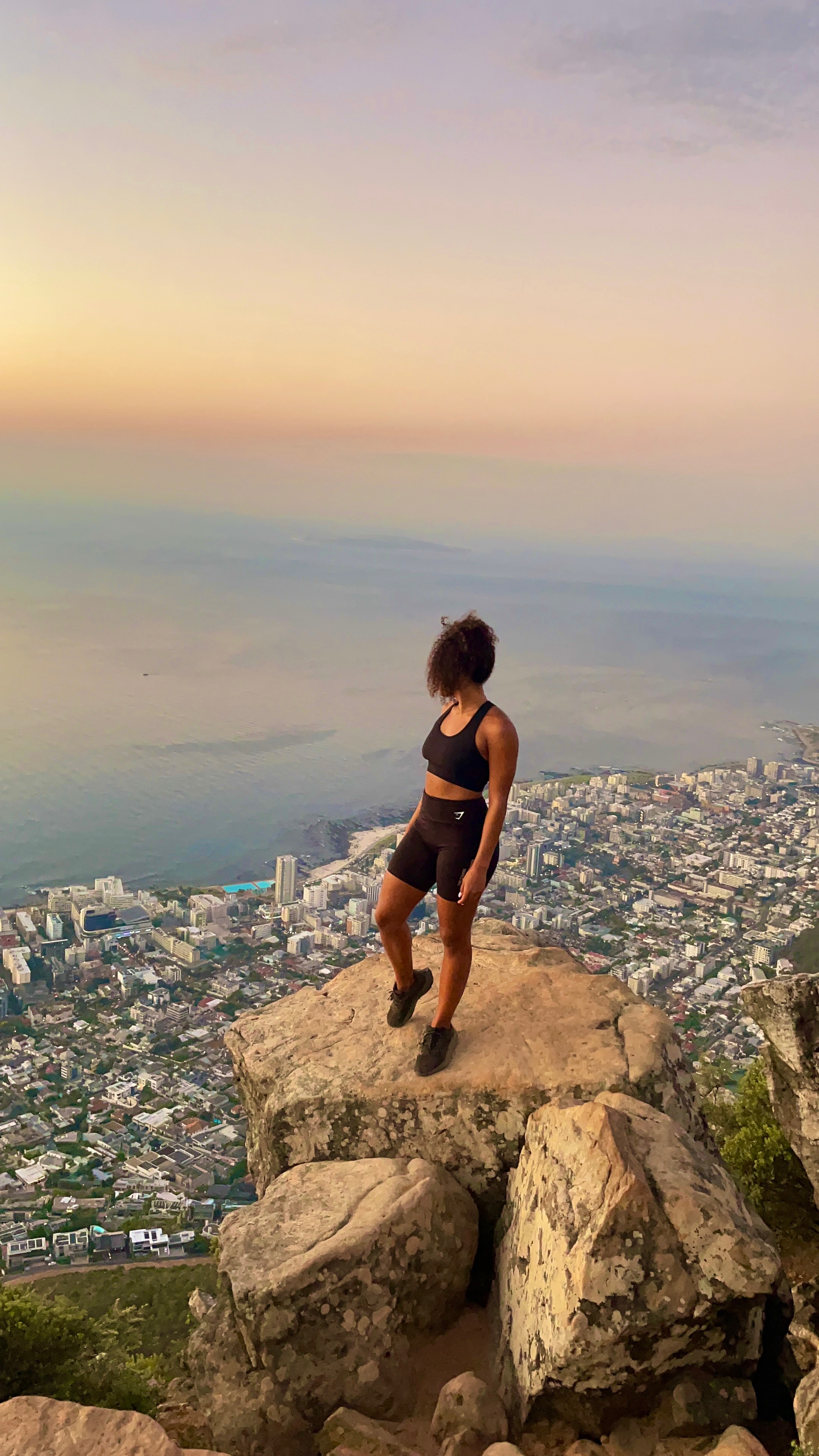 Taliya on a rocky peak overlooking a coastal city at golden hour