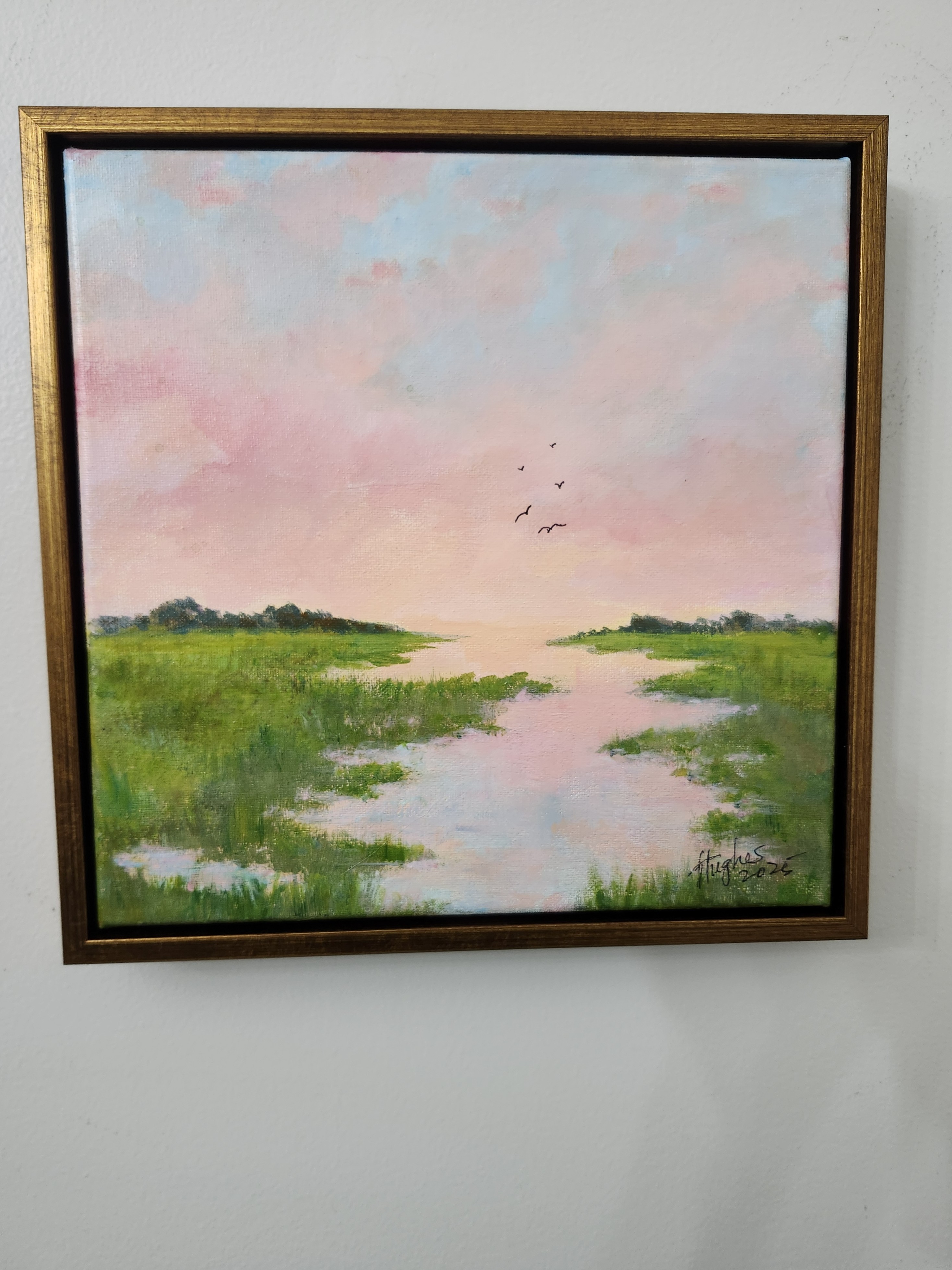 Framed marsh painting at dusk with a central waterway reflecting a soft pink and violet sky, green grasses, silhouetted treelines and five birds in flight.