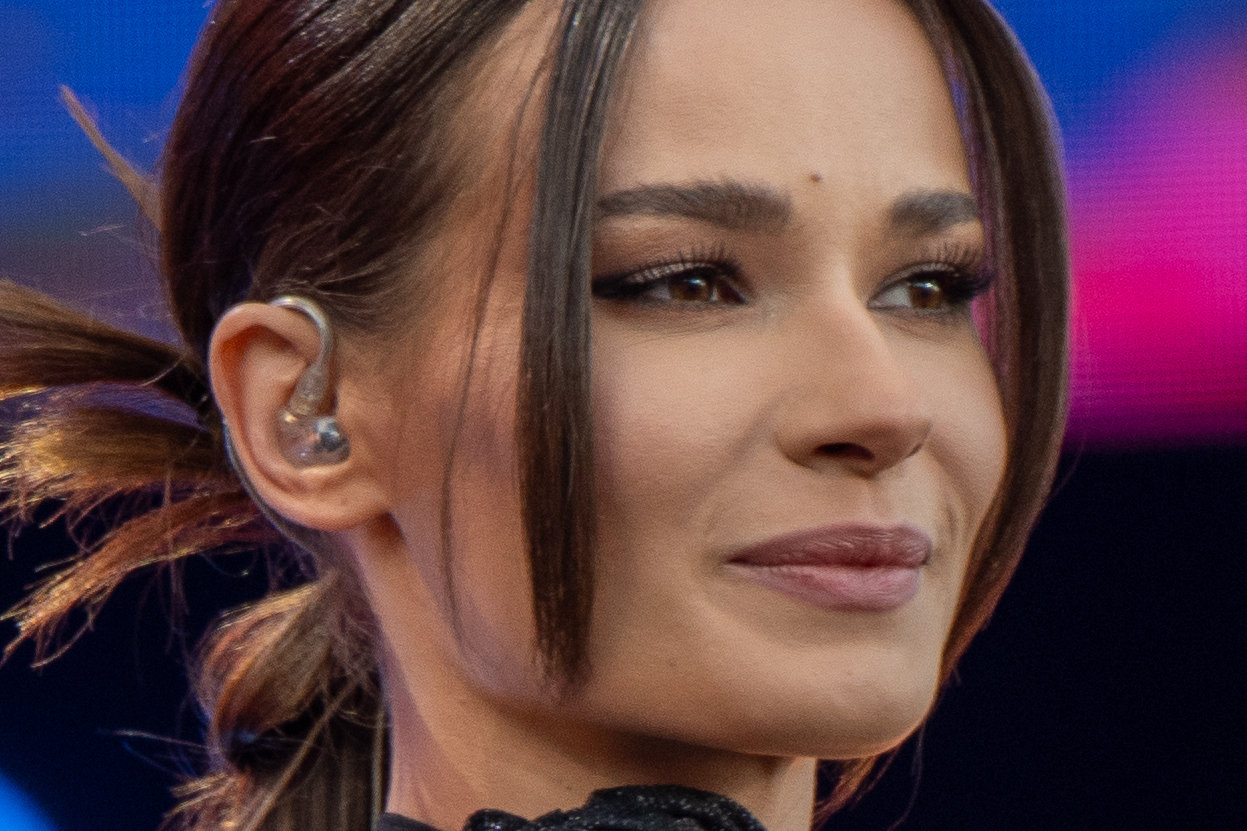 Natalia Szroeder z ciemnymi włosami spiętymi w kucyk i czarnym chokerem podczas koncertu na scenie