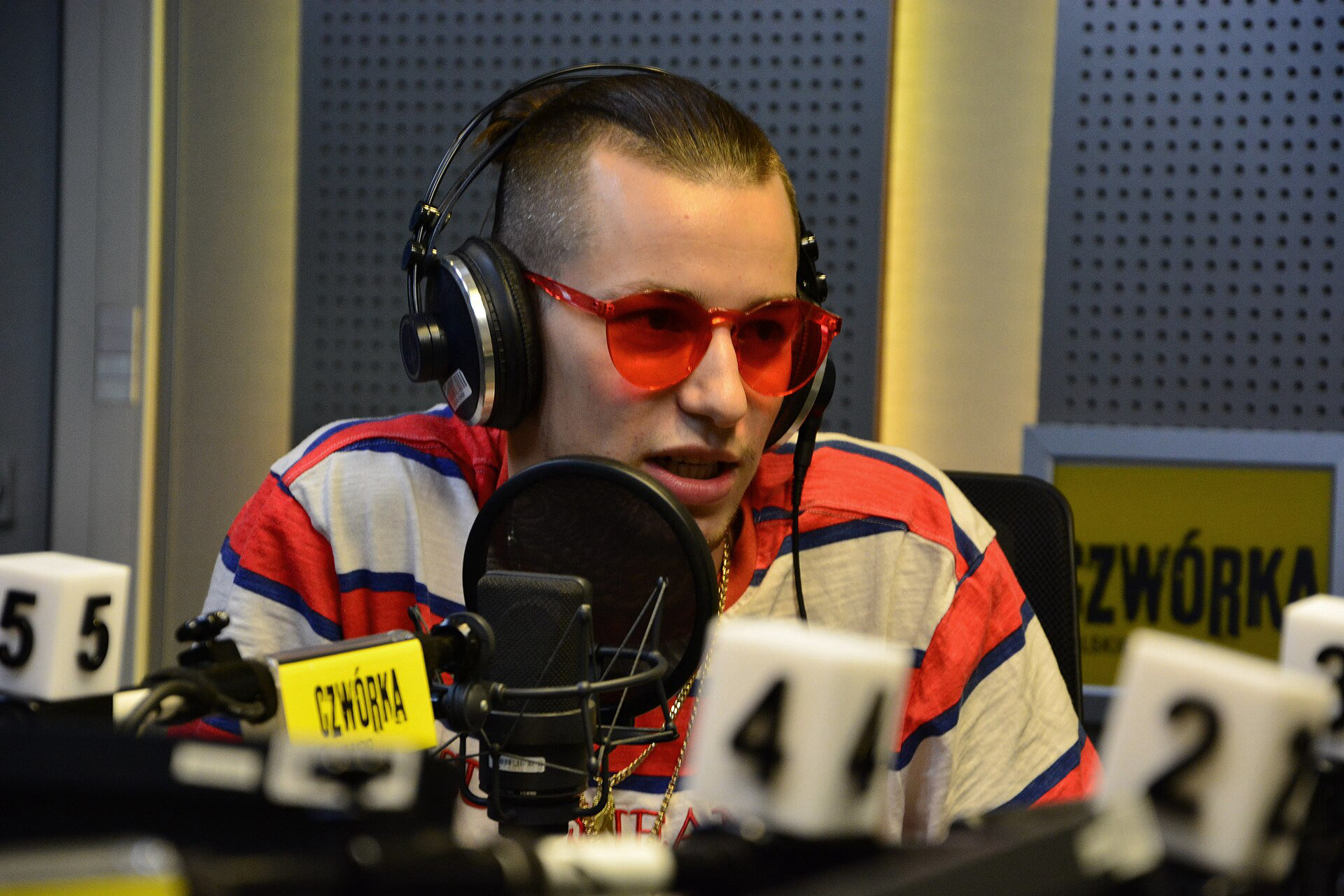 Żabson w czerwonych okularach i słuchawkach przy mikrofonie w studiu radiowym podczas wywiadu
