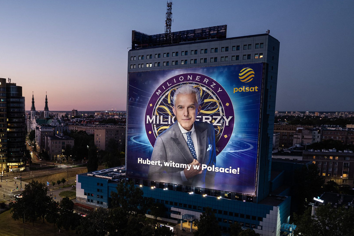 Wielkoformatowa reklama Polsatu z „Milionerami” na wieżowcu w Warszawie o zmierzchu