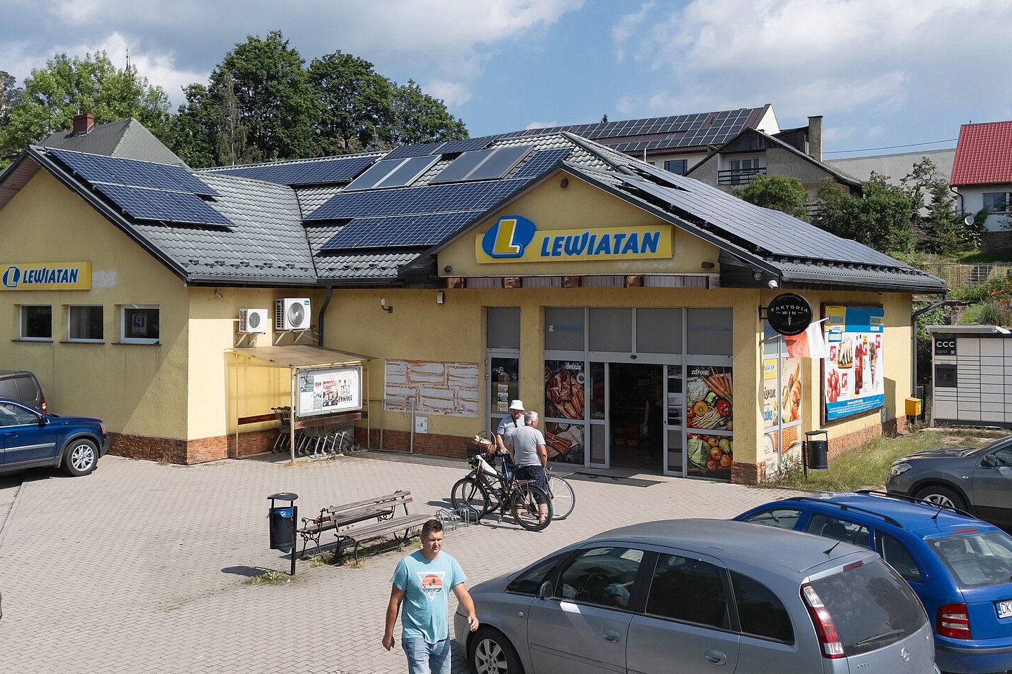 Sklep Lewiatan w Szczytnej z żółtą fasadą, szyldami sieci i panelami fotowoltaicznymi na dachu, przed nim parking