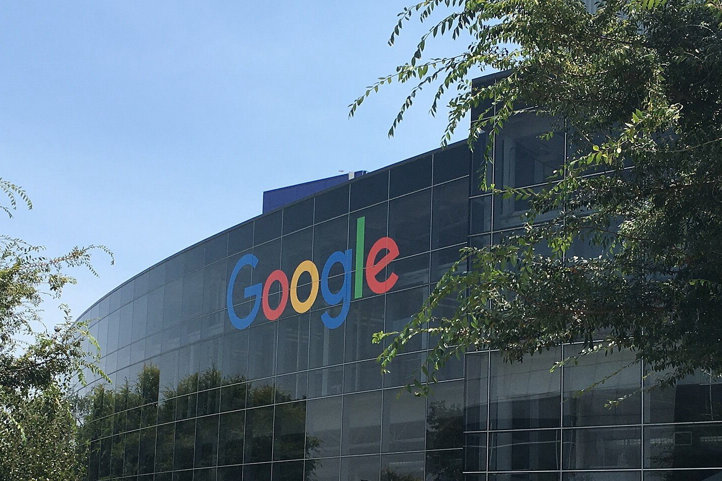 Szklana fasada siedziby Google w Mountain View z dużym kolorowym logo Google, otoczona zielenią i trawami