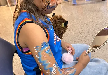Child with basketball face paint and airbrushed arm design at an Oklahoma City event