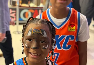 Two children in OKC Thunder jerseys with matching mascot face paint