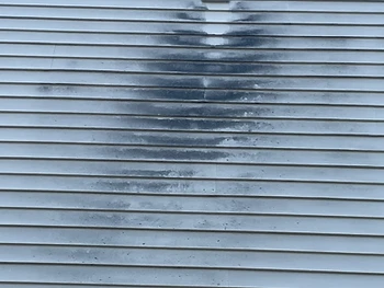 Vinyl siding with dark mildew around a wall vent, before cleaning