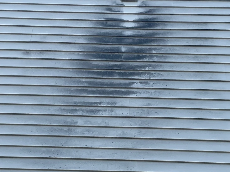 Vinyl siding with dark mildew around a wall vent, before cleaning