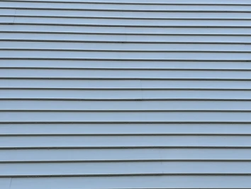 Clean vinyl siding and wall vent along the roofline of a New England home