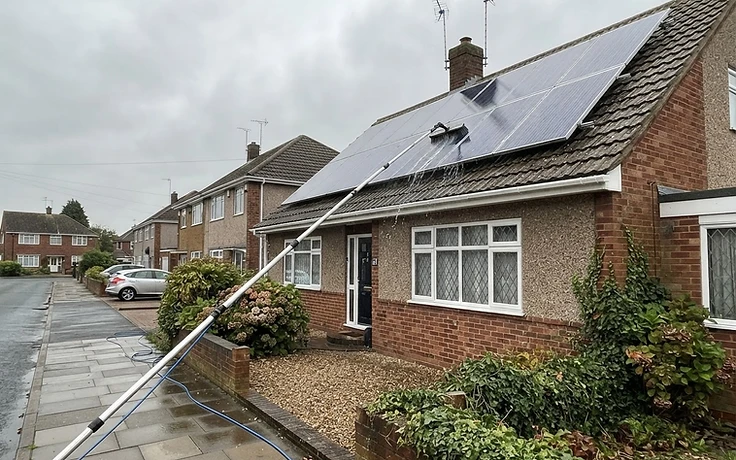 Water-fed pole reaching solar panels on a two storey house roof from ground level