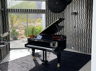 Black grand piano in a desert home interior with mountain views through sliding glass doors