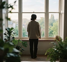Person standing at a bright window with plants in the foreground
