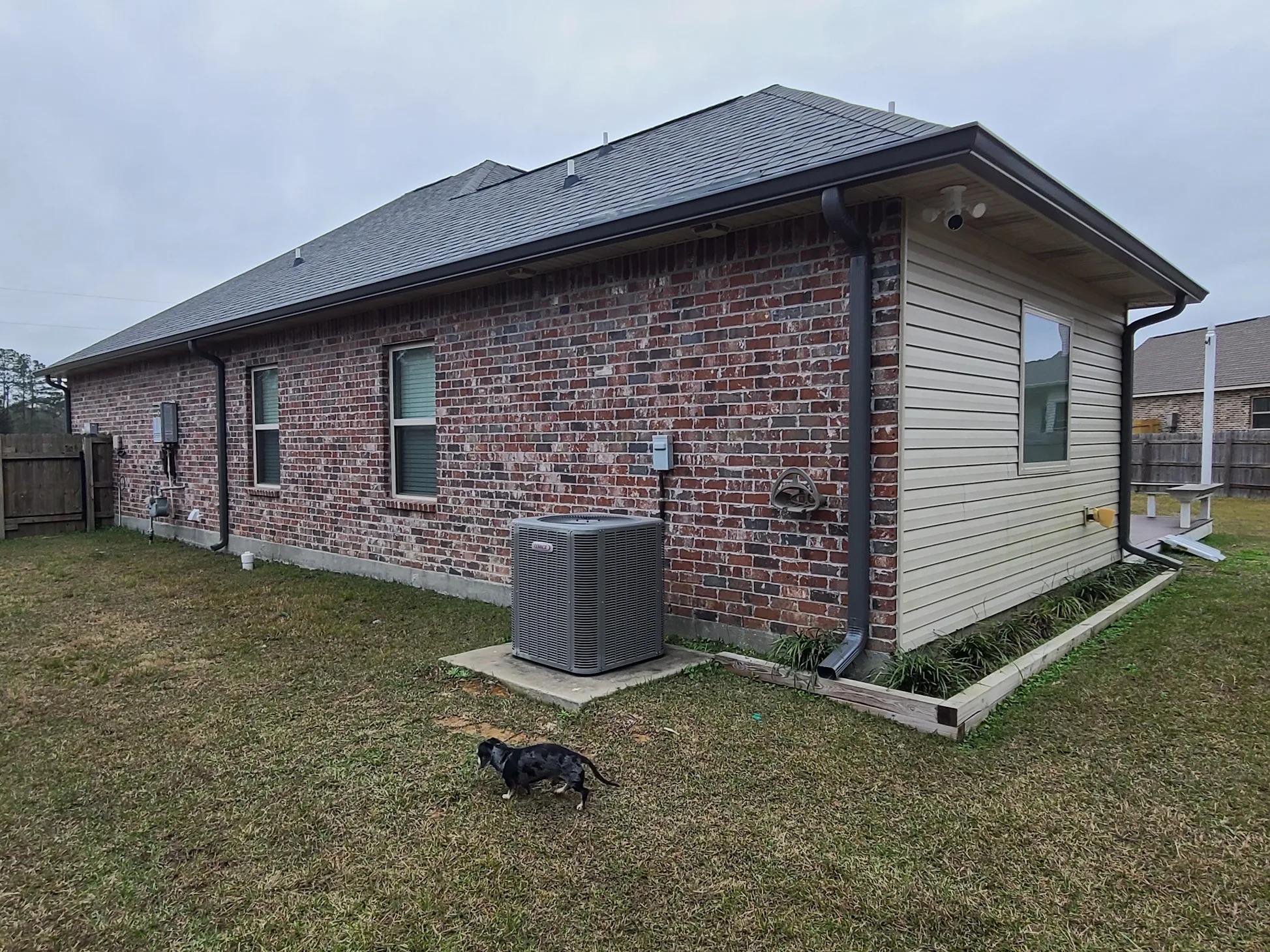 Black gutters and downspouts across a brick home's back elevation