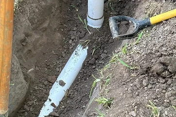 Trench with buried downspout drain pipe and pop-up emitter riser