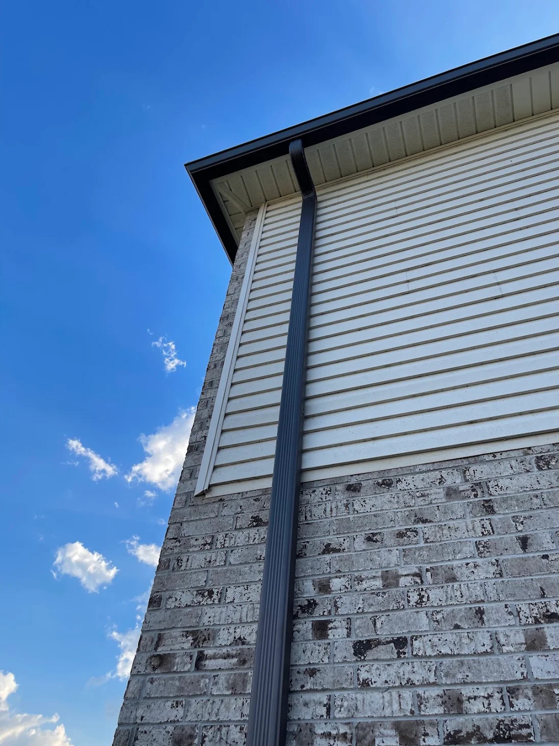 Downspout running up a brick and siding wall