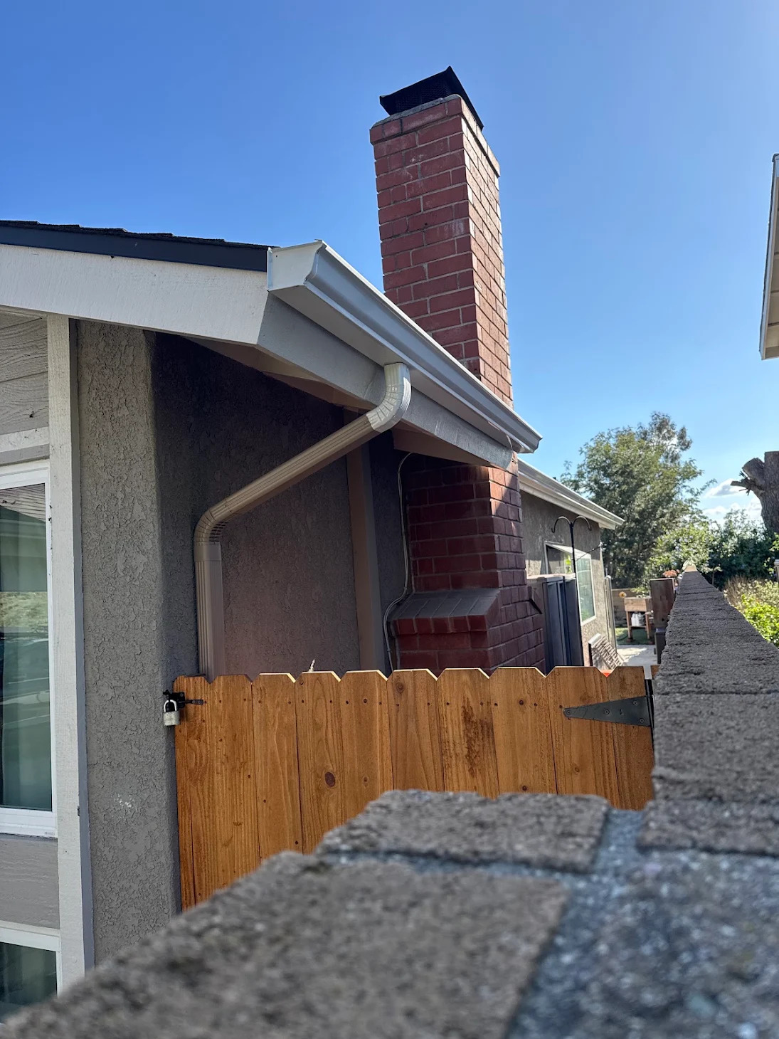 White gutter and downspout beside a brick chimney