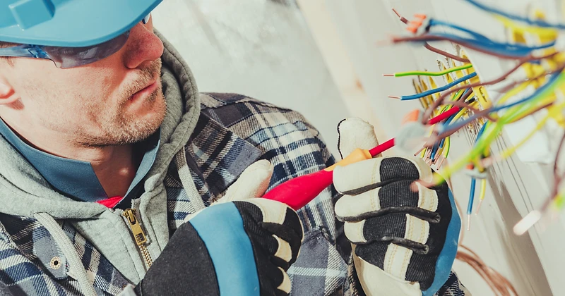 A licensed electrician in a hard hat working on home wiring at a junction box