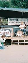 Photographer kneeling to shoot a banjo player on the wooden stage at JescoFest 2006