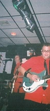 Guitarist in a red shirt playing a seafoam electric guitar indoors at JescoFest 2006