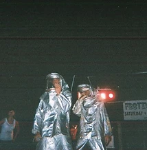 8-BIT performing on stage in silver fire suits with Festival of the Rivers banner at JescoFest 2006