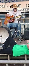 Jesco White lying on the stage edge playing harmonica with J. Glenn on guitar at JescoFest 2006