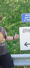 Man pointing at a hand-lettered Jescofest 2006 sign by the road