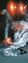 8-BIT member kneeling in a silver fire suit eating chips on stage at JescoFest 2006