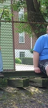 Two men sitting on a wooden rail by a chain-link fence at JescoFest 2006