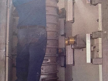 Worker assembling a tall ribbed column inside a metal enclosure