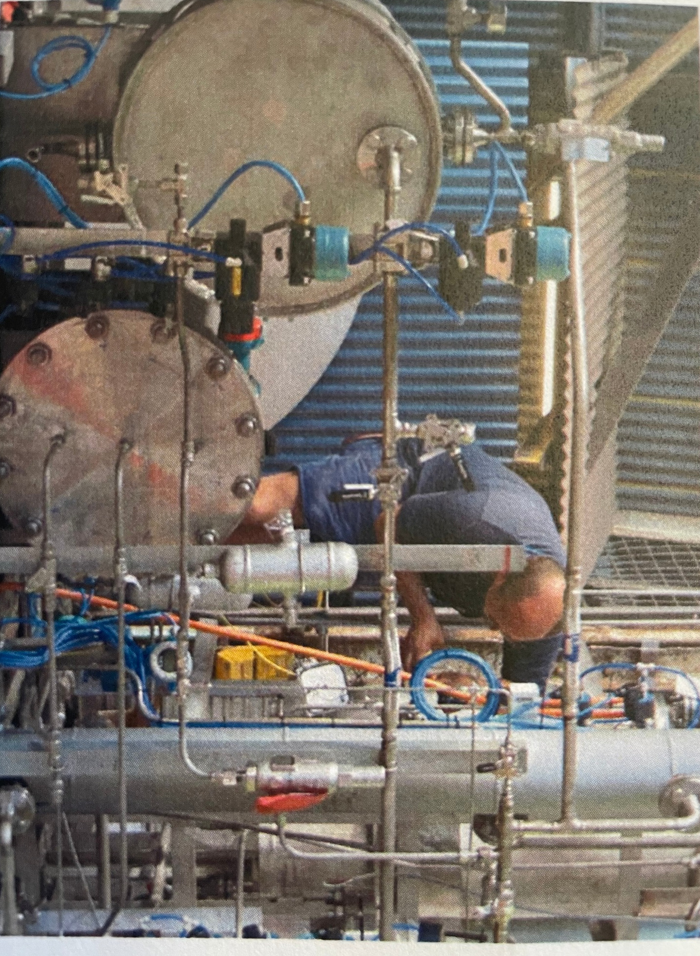 Technician working on industrial pipework, valves and hoses in a workshop