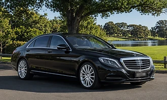 A black Mercedes-Benz S-Class sedan parked on a driveway beside a lake