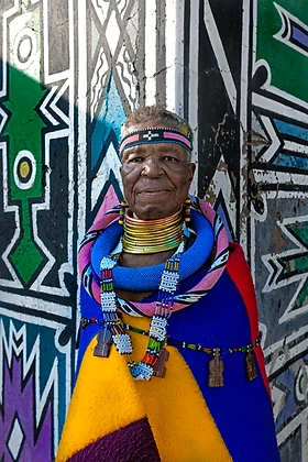 Portrait of Esther Mahlangu before a weathered Ndebele wall, by Clint Strydom