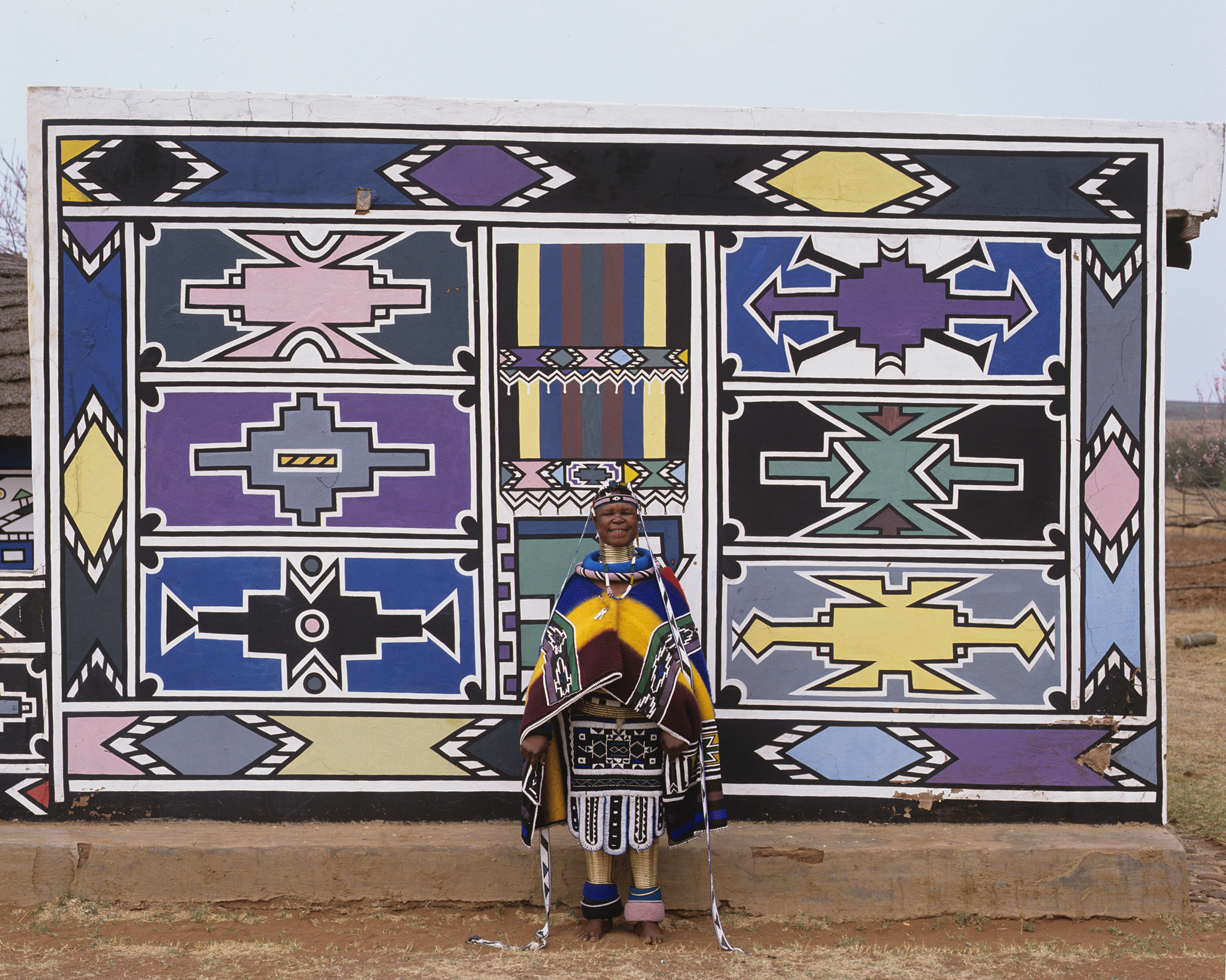 Esther Mahlangu before a completed Ndebele mural wall at Botshabelo