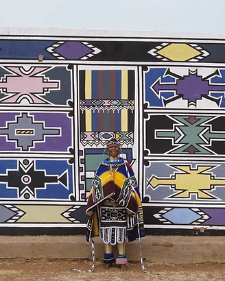 Esther Mahlangu before a completed Ndebele mural wall at Botshabelo