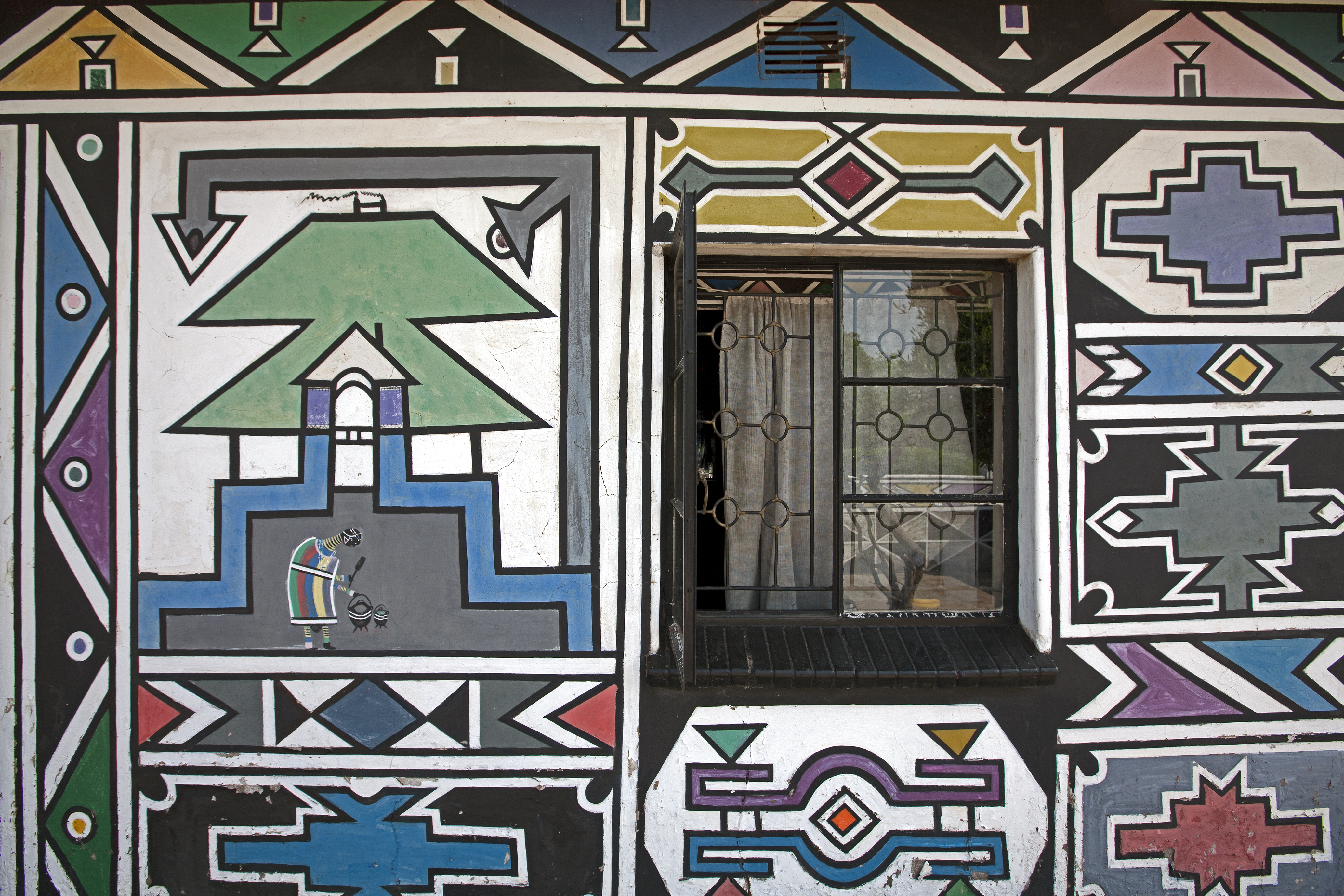 A Ndebele mural wall painted by Dr Esther Mahlangu, with a window and figurative motif