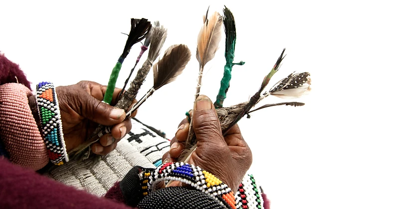 Dr Esther Mahlangu's hands holding ceremonial feathered wands and beaded bracelets, by Clint Strydom