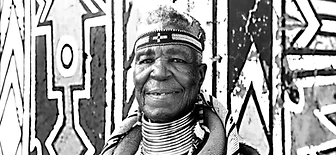 Black-and-white portrait of Esther Mahlangu before a mural, by Clint Strydom